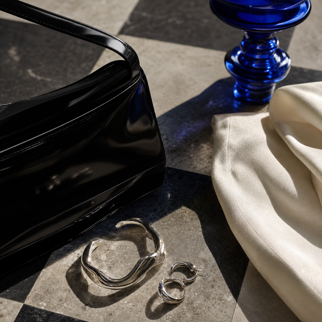 Black handbag, silver jewelry and cobalt glass styled as a luxury still life